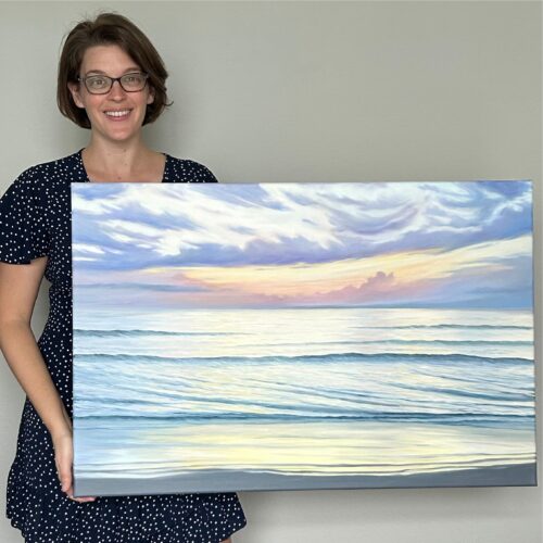 Artist holding a painting of the ocean lit by a glowing sunrise